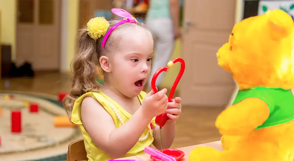 little girl with down syndrome using toy stethoscope on teddy