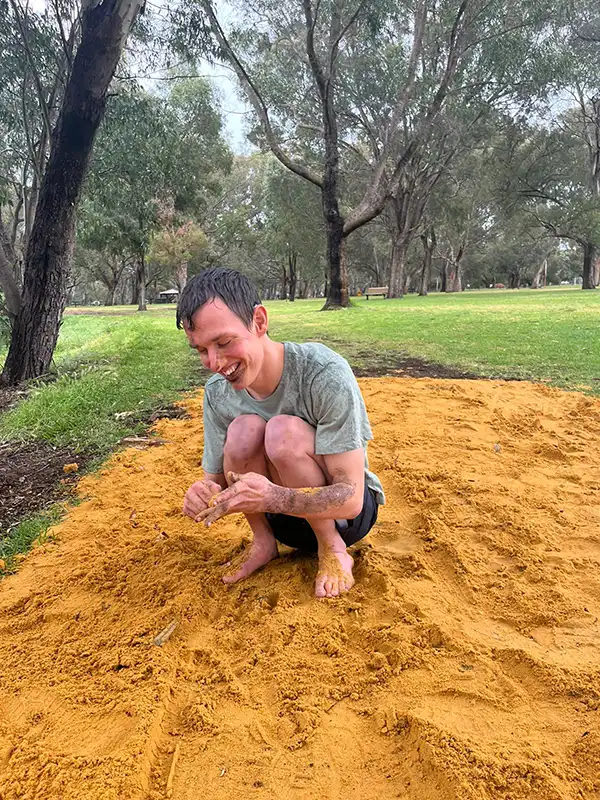 A young man with intellectual disability in a park, playing in the sand